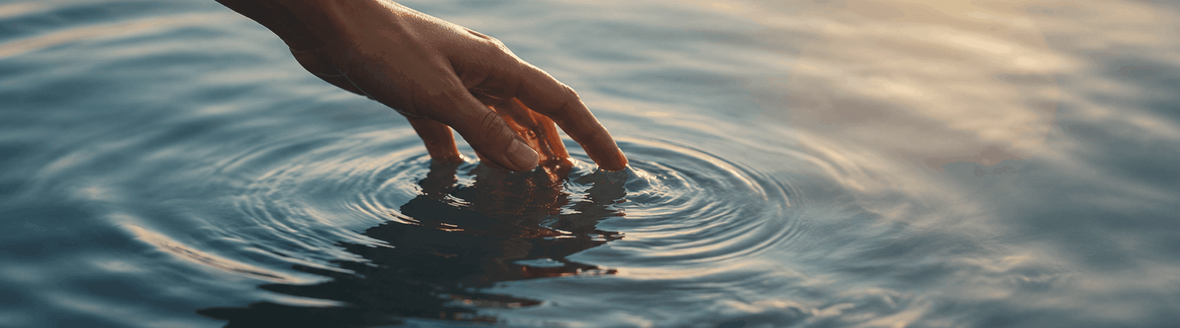 Photo - Fingers touching the water’s surface, creating ripples.